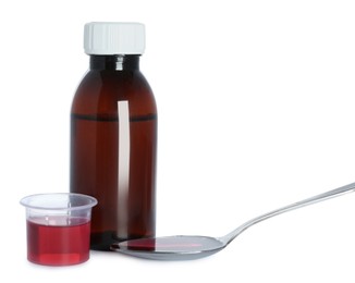 Bottle of cough syrup, spoon and measuring cup on white background