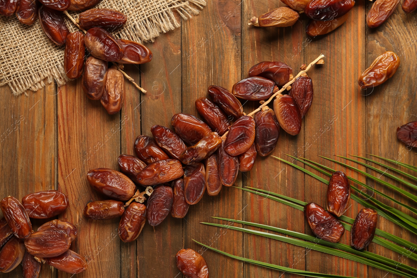 Photo of Branches with sweet dried dates and green leaf on wooden table, flat lay