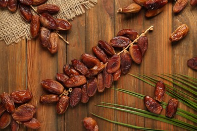 Photo of Branches with sweet dried dates and green leaf on wooden table, flat lay