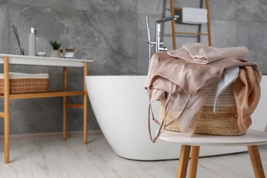Photo of Wicker laundry basket with clothes on stool in bathroom