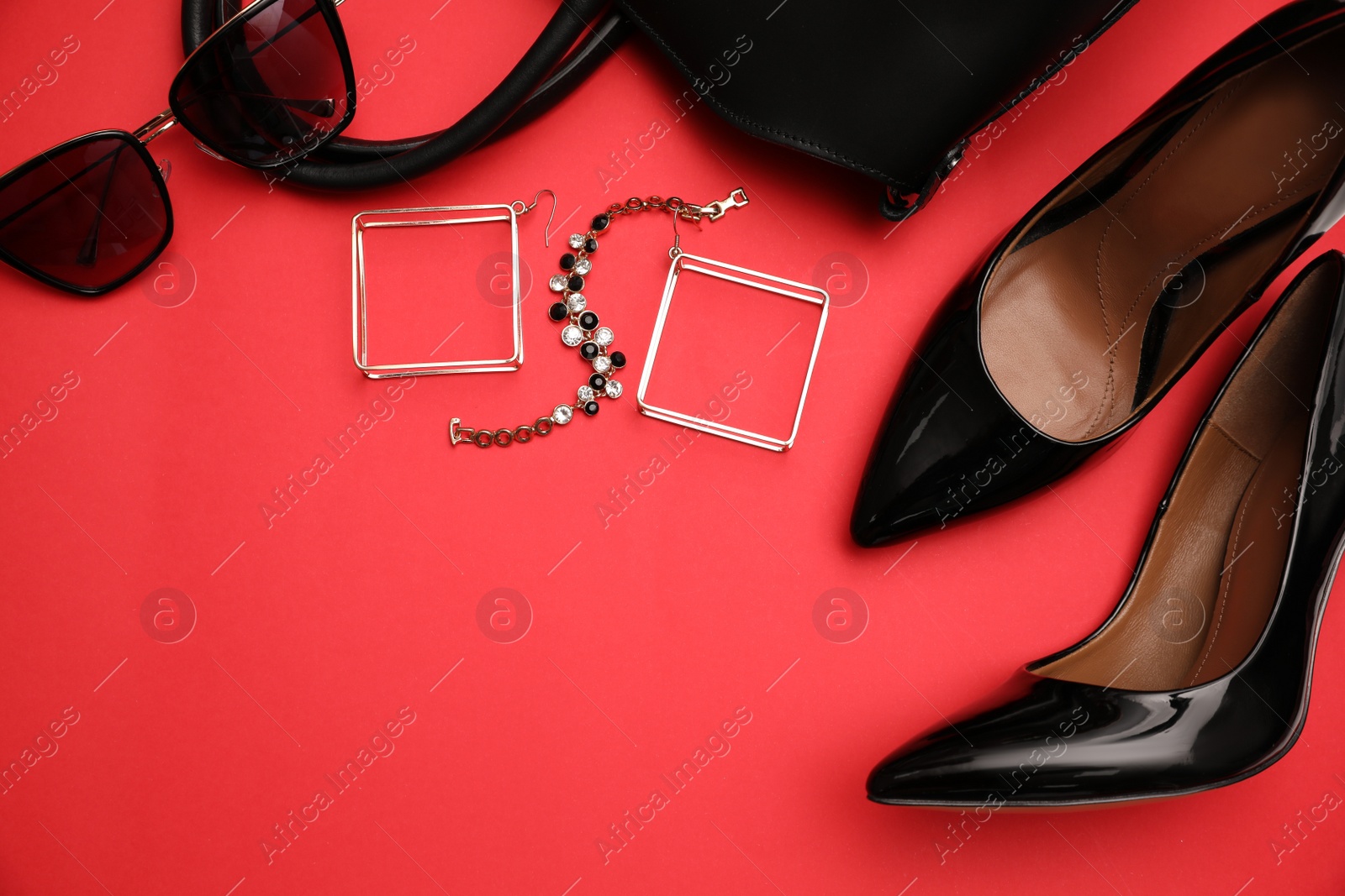 Photo of High heel shoes, bag and accessories on red background, flat lay. Space for text