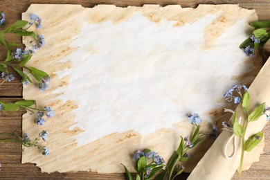Photo of Beautiful forget-me-not flowers and sheets of old parchment paper on wooden table, top view