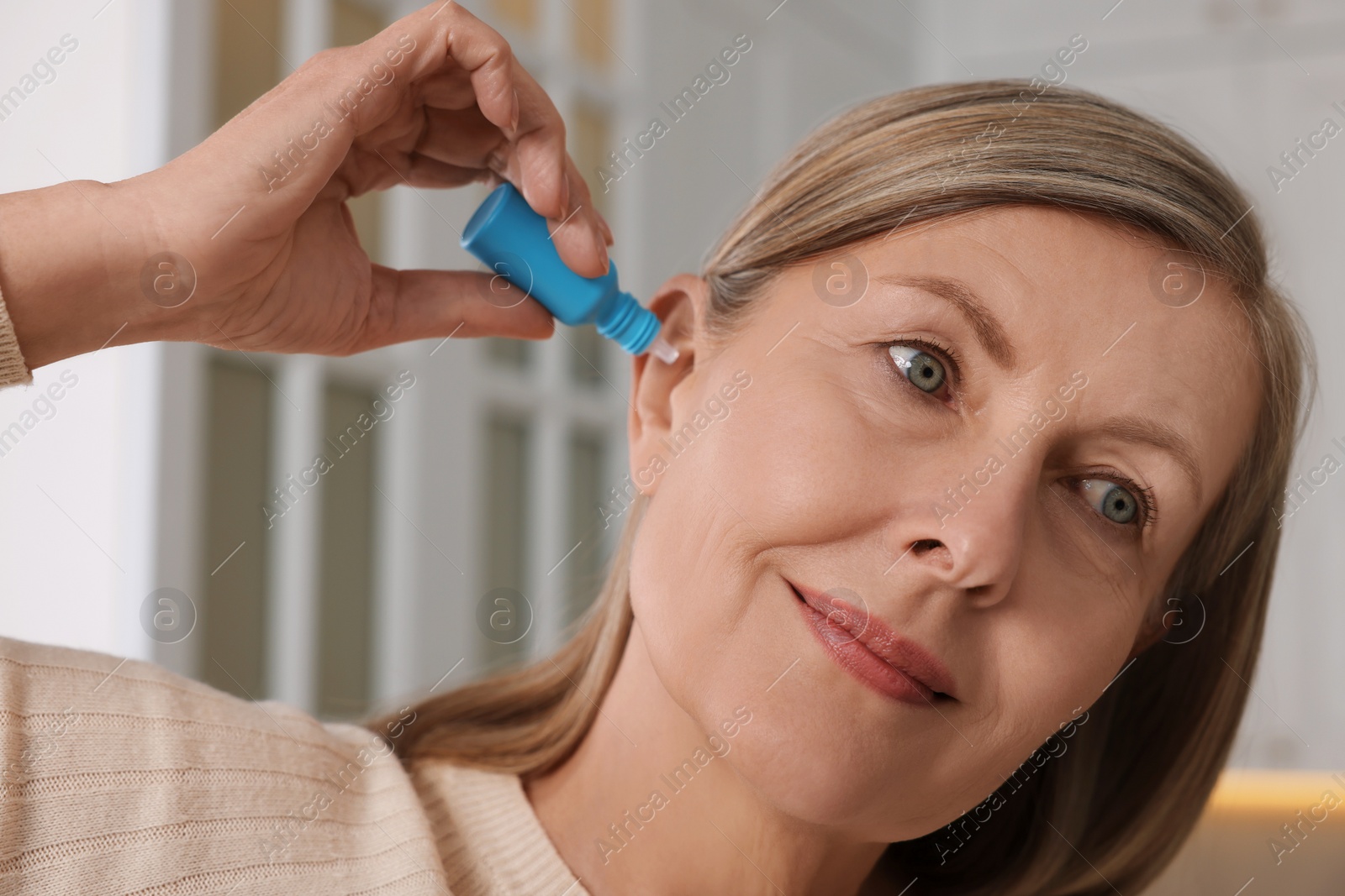 Photo of Woman applying medical ear drops at home