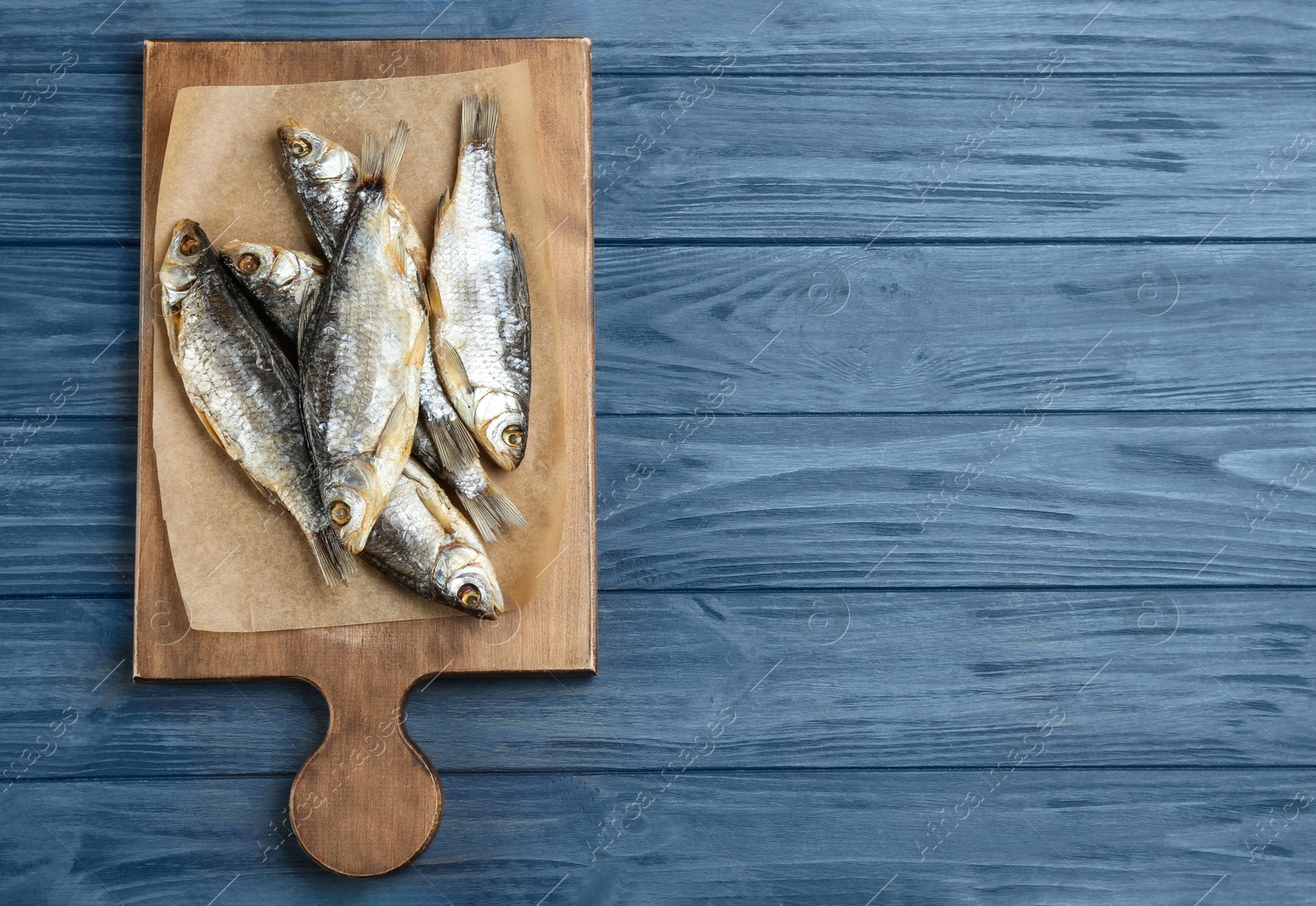 Photo of Tasty dried fish on blue wooden table, top view. Space for text