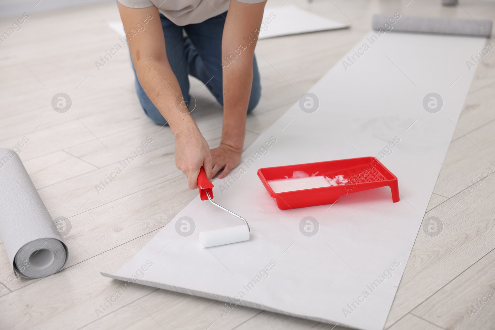 Photo of Man applying glue onto wallpaper sheet in room, closeup