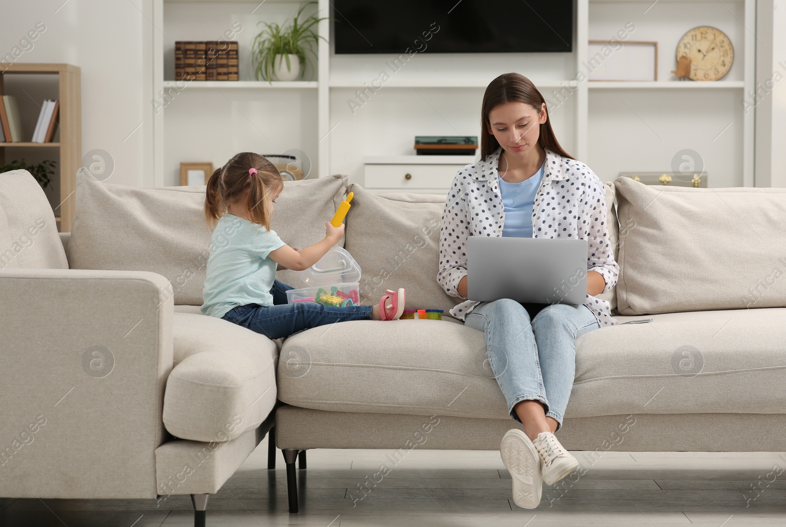 Photo of Little daughter playing while her mother working remotely on sofa at home