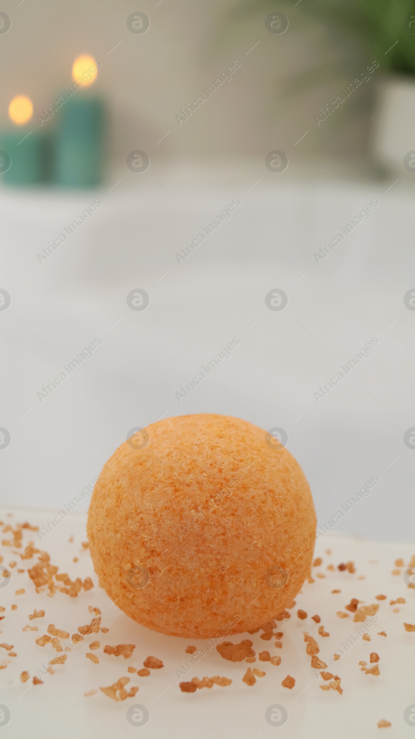 Photo of Orange bath bomb with salt on countertop near tub indoors. Bokeh effect