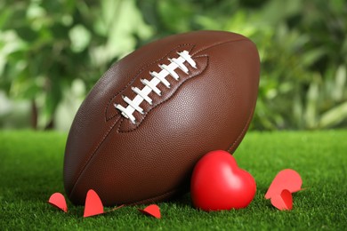 American football ball and hearts on green grass against blurred background