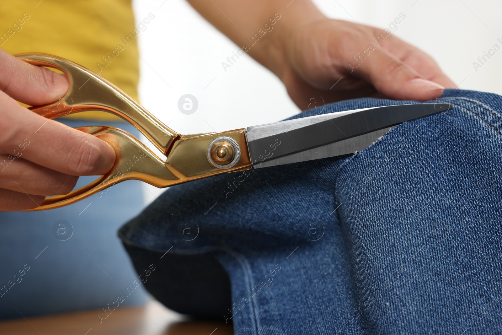 Photo of Woman cutting jeans with scissors at wooden table indoors, closeup