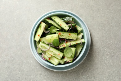 Photo of Delicious cucumber salad with onion and spinach in bowl on grey background, top view