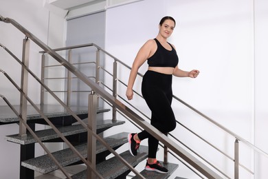 Overweight woman in sportswear running downstairs indoors