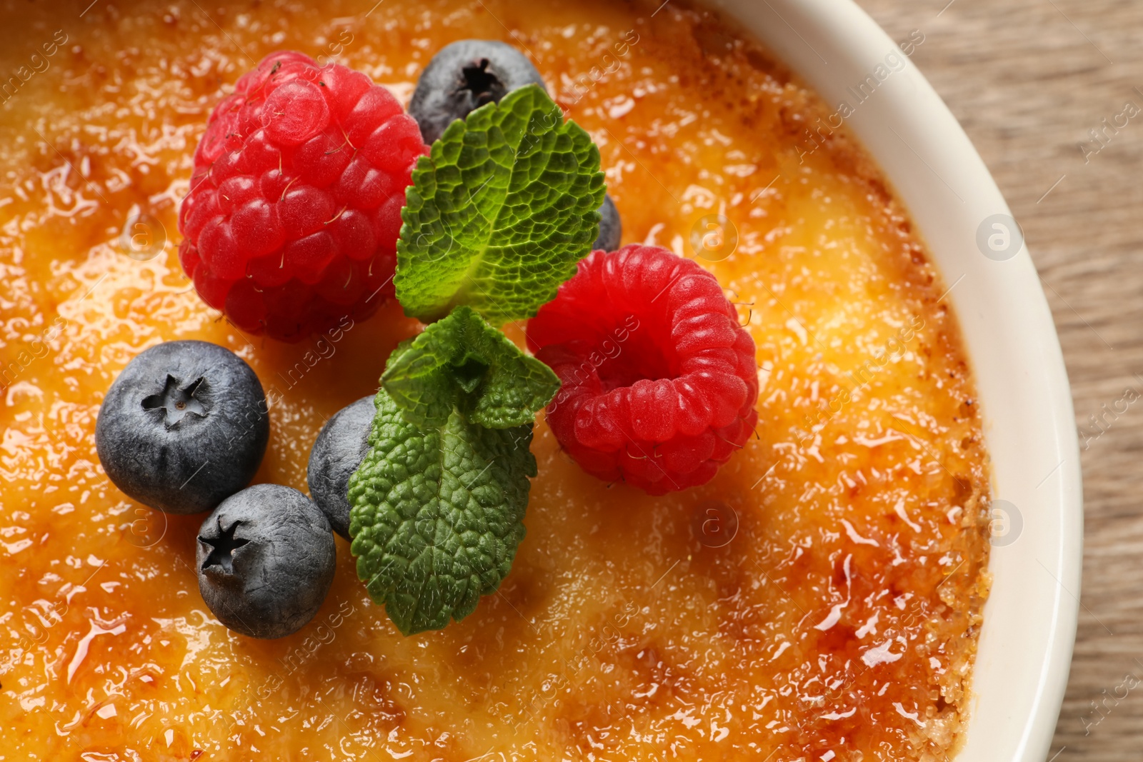 Photo of Delicious creme brulee with fresh berries on wooden table, closeup