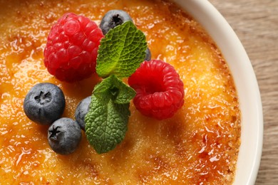 Photo of Delicious creme brulee with fresh berries on wooden table, closeup