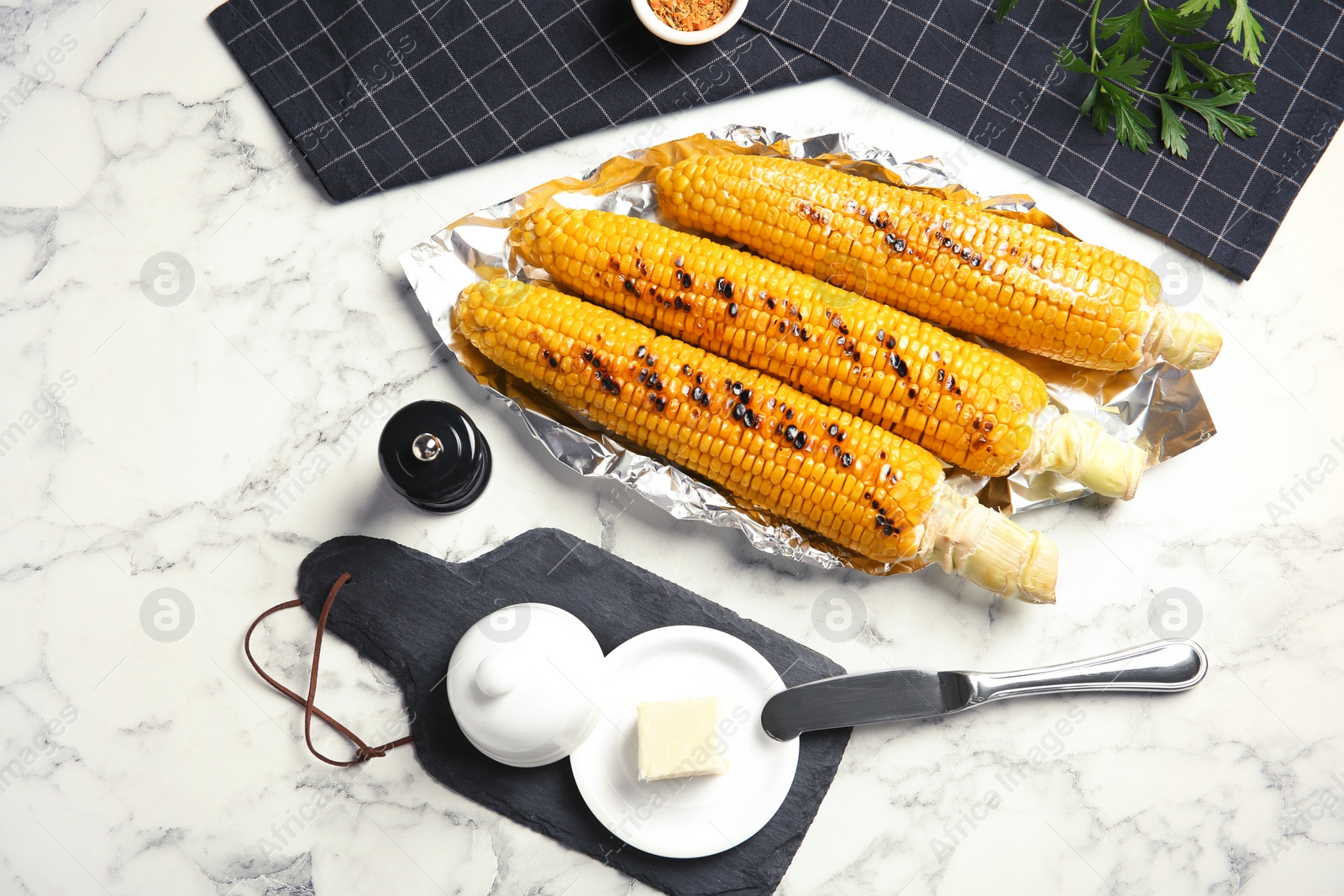 Photo of Fresh grilled tasty corn cobs served with butter on marble table, top view