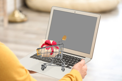 Image of Woman shopping online using laptop, small cart with box on computer