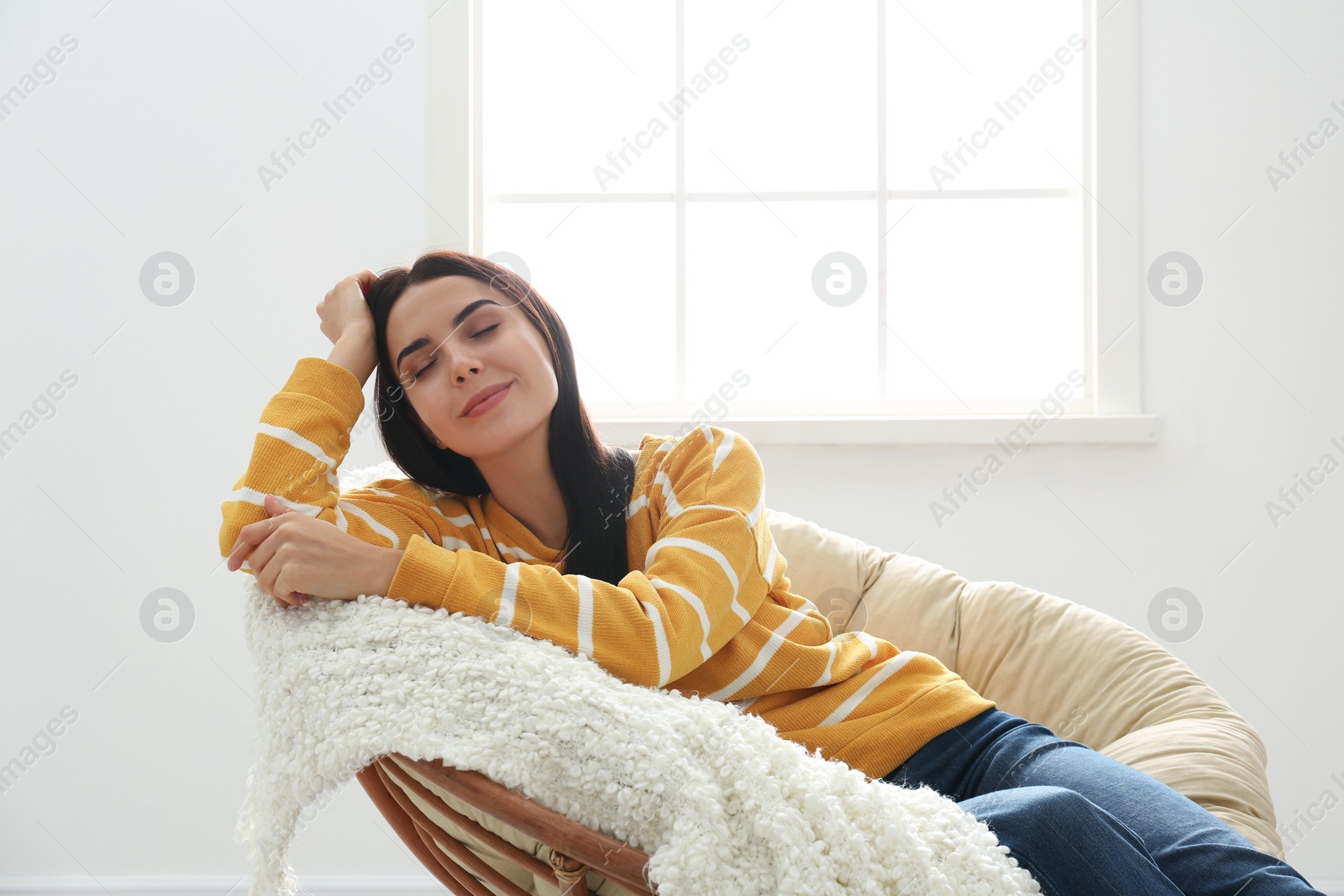 Photo of Young woman relaxing in papasan chair near window at home