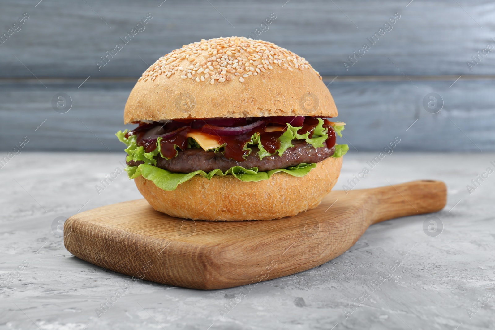 Photo of Delicious cheeseburger with ketchup and patty on grey textured table