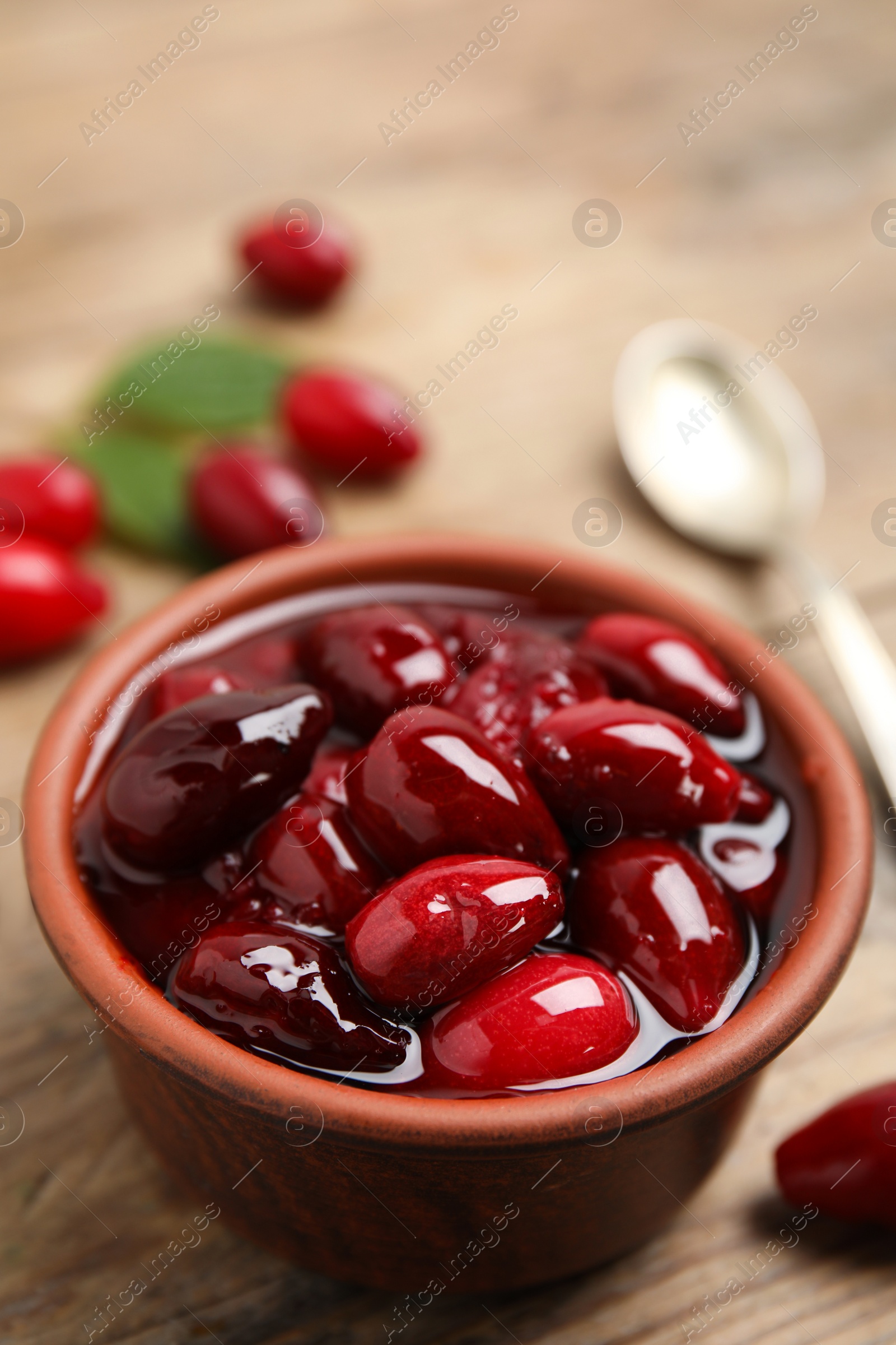 Photo of Delicious dogwood jam with berries in bowl on wooden table, closeup