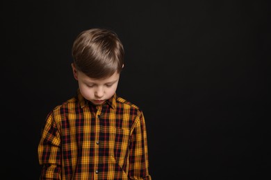 Photo of Upset boy on black background, space for text. Children's bullying