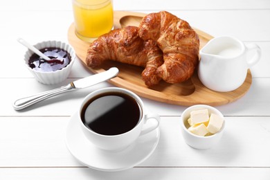 Photo of Fresh croissants, butter, jam and coffee on white wooden table. Tasty breakfast