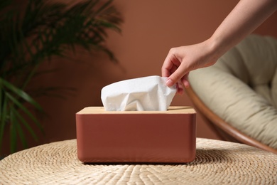 Photo of Woman taking paper tissue out of box on table indoors, closeup