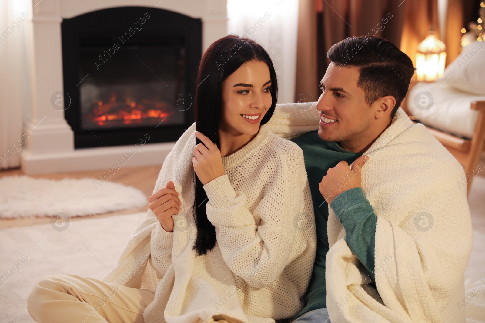 Photo of Couple covered in plaid sitting near fireplace at home