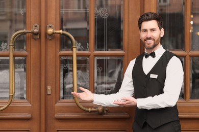Butler in elegant suit near wooden hotel door. Space for text