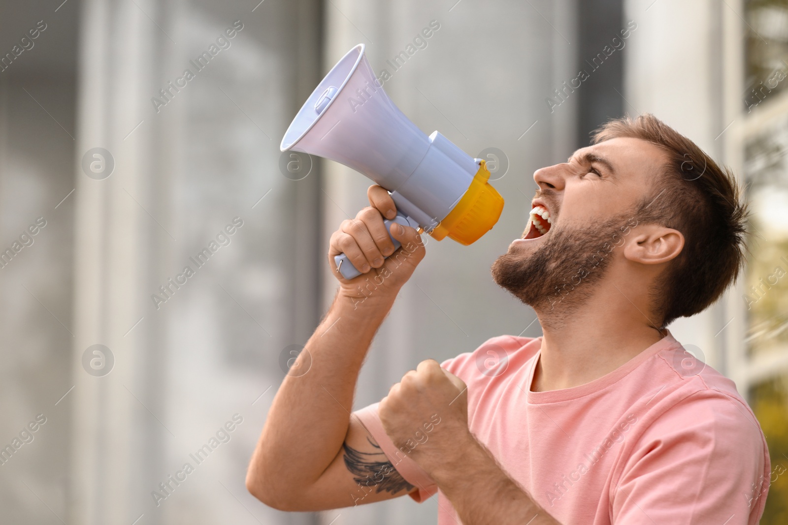 Image of Emotional young man with megaphone outdoors. Protest leader