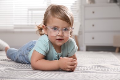 Cute little girl in glasses on floor at home. Space for text