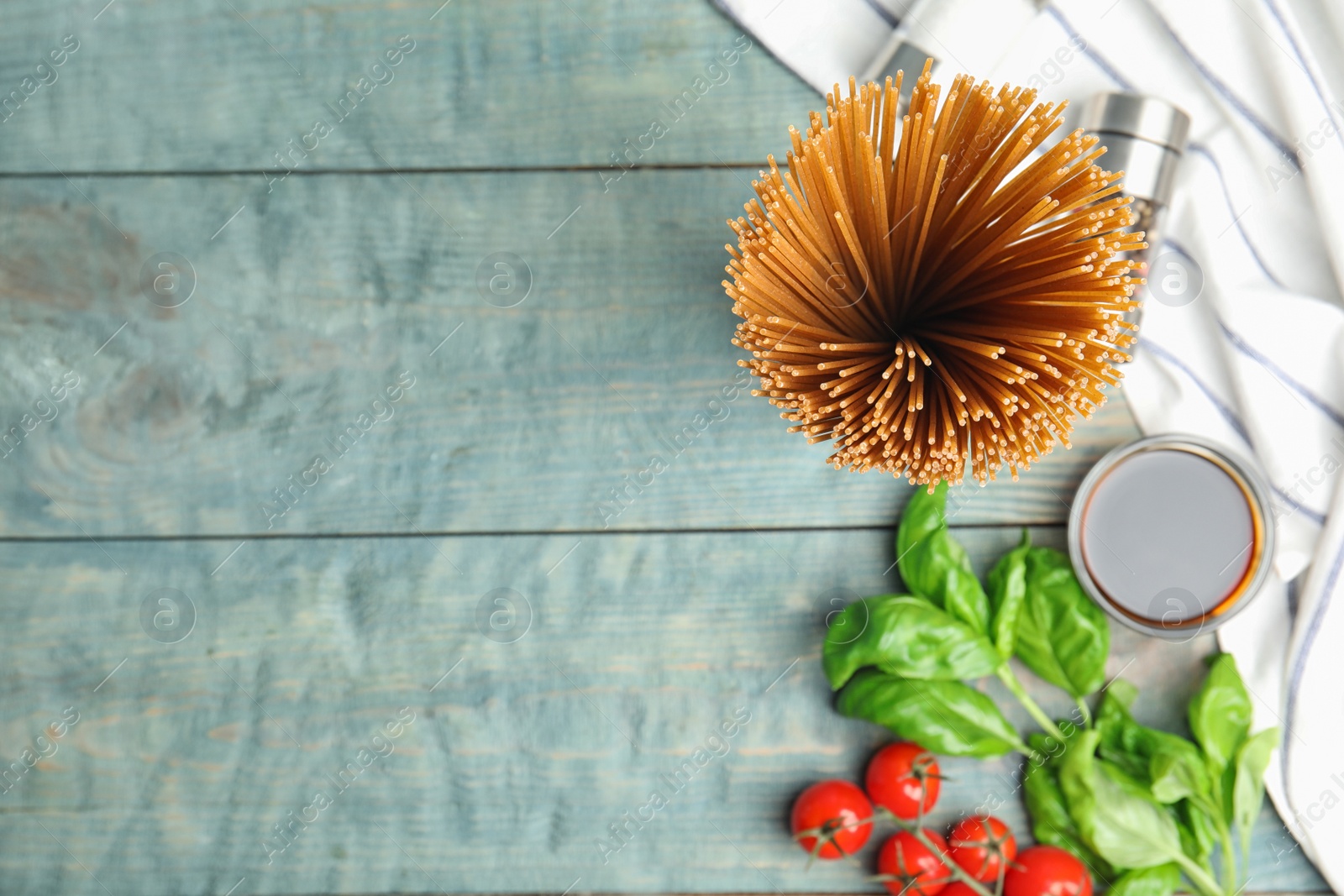 Photo of Uncooked buckwheat noodles and fresh ingredients on blue wooden table, flat lay. Space for text