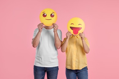 People covering faces with emoticons on pink background