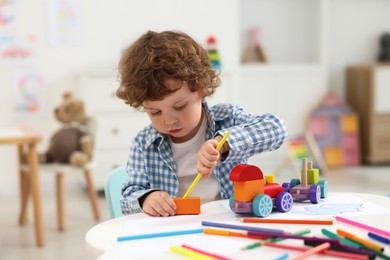 Photo of Cute little boy playing with wooden toys at white table in kindergarten
