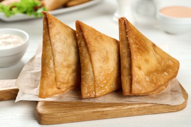 Fresh delicious crispy samosas on white wooden table, closeup