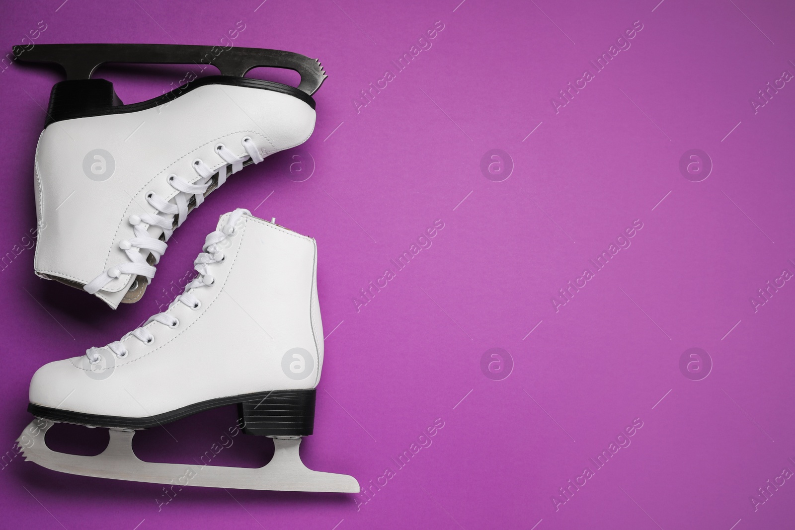 Photo of Pair of figure ice skates on purple background, flat lay. Space for text