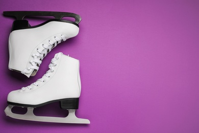 Photo of Pair of figure ice skates on purple background, flat lay. Space for text