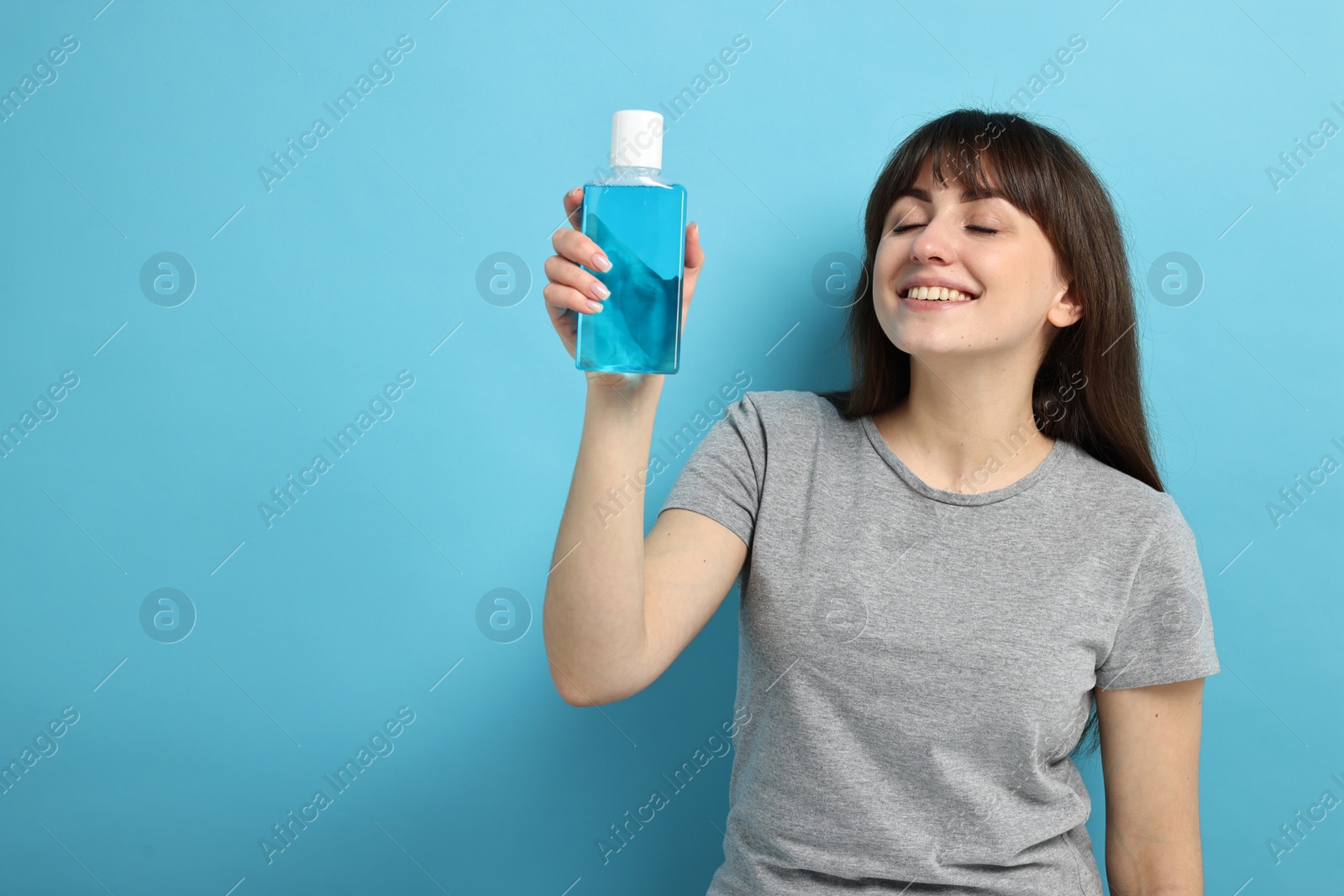 Photo of Young woman with mouthwash on light blue background, space for text