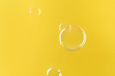 Photo of Beautiful transparent soap bubbles on yellow background