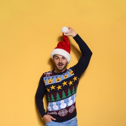 Photo of Young man in Christmas sweater and hat on color background