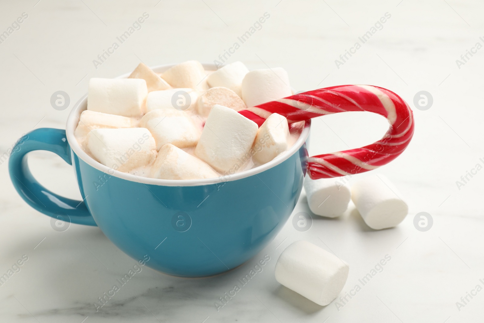 Photo of Tasty hot chocolate with marshmallows and candy cane on white marble table, closeup