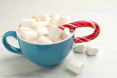 Tasty hot chocolate with marshmallows and candy cane on white marble table, closeup