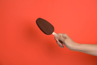 Photo of Woman holding ice cream glazed in chocolate on red background, closeup