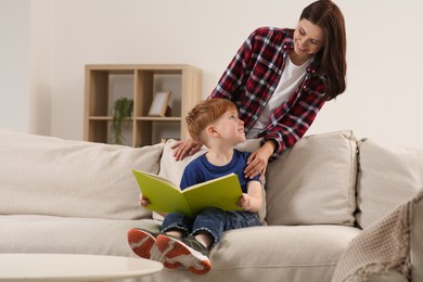 Happy mother reading book with her child at home, space for text