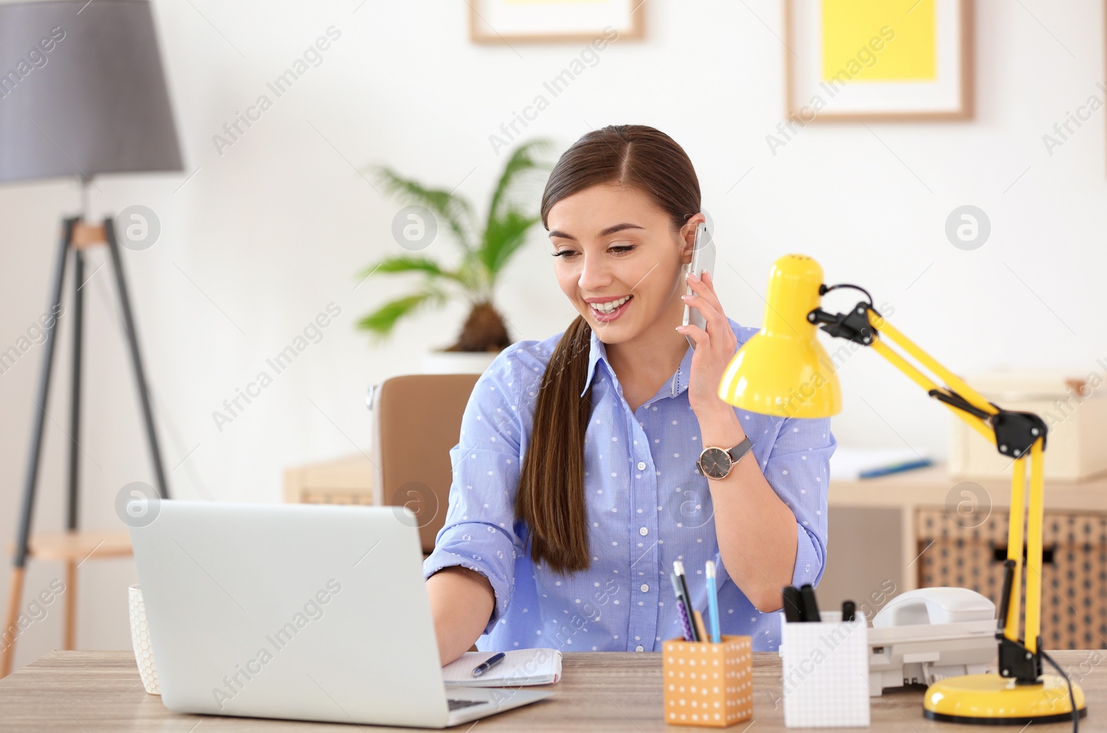 Photo of Young woman talking on phone at workplace