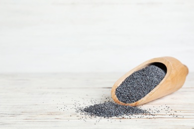 Photo of Wooden scoop with poppy seeds on table. Space for text