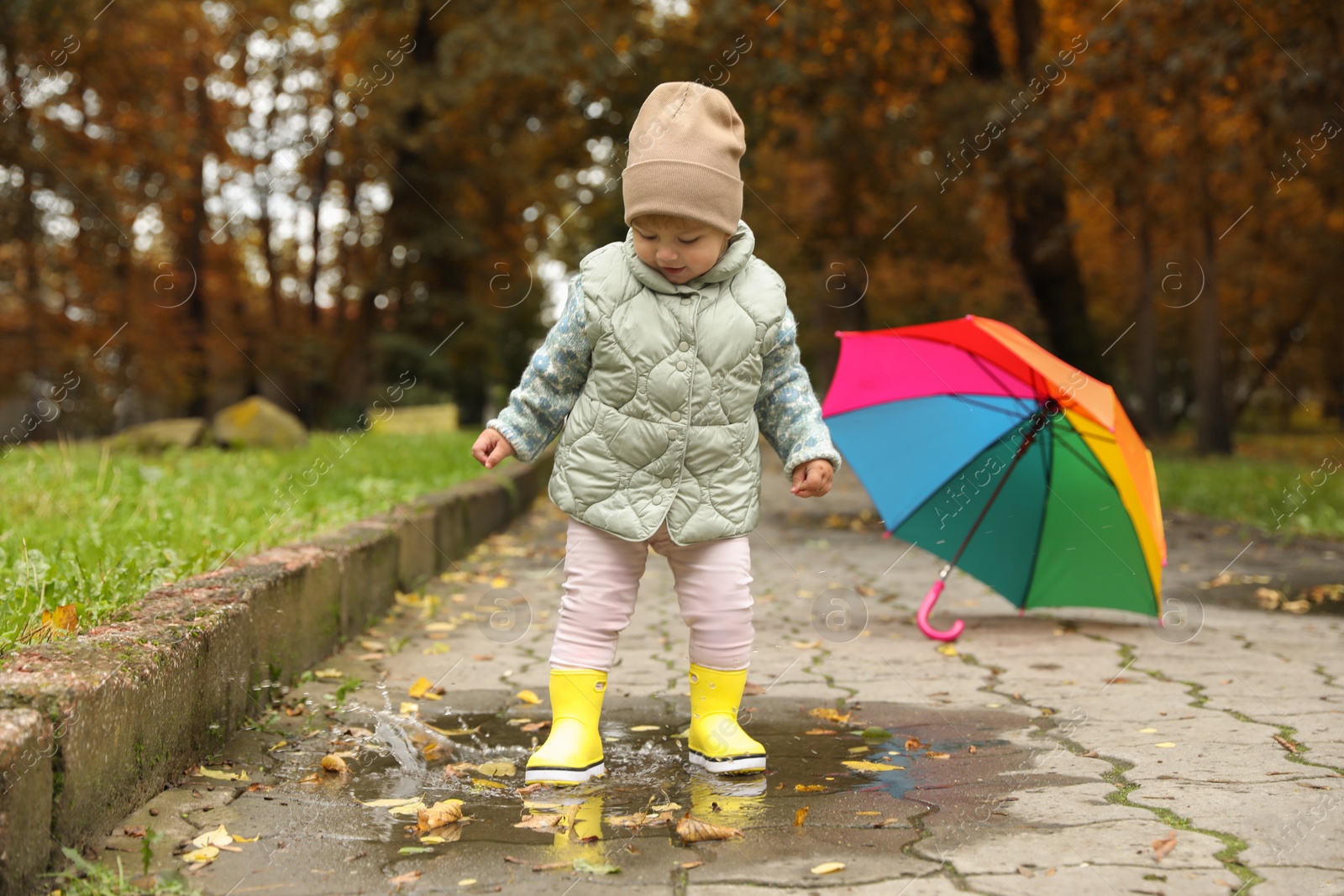 Photo of Cute little girl standing in puddle near colorful umbrella outdoors