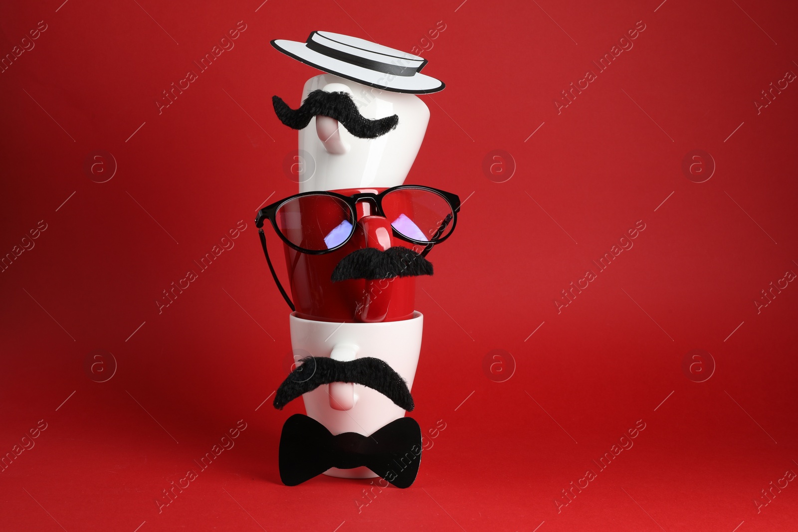 Photo of Men's faces made of cups, fake mustaches, glasses, hat and bow tie on red background