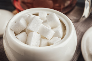 Photo of Refined sugar cubes in ceramic bowl on table, closeup