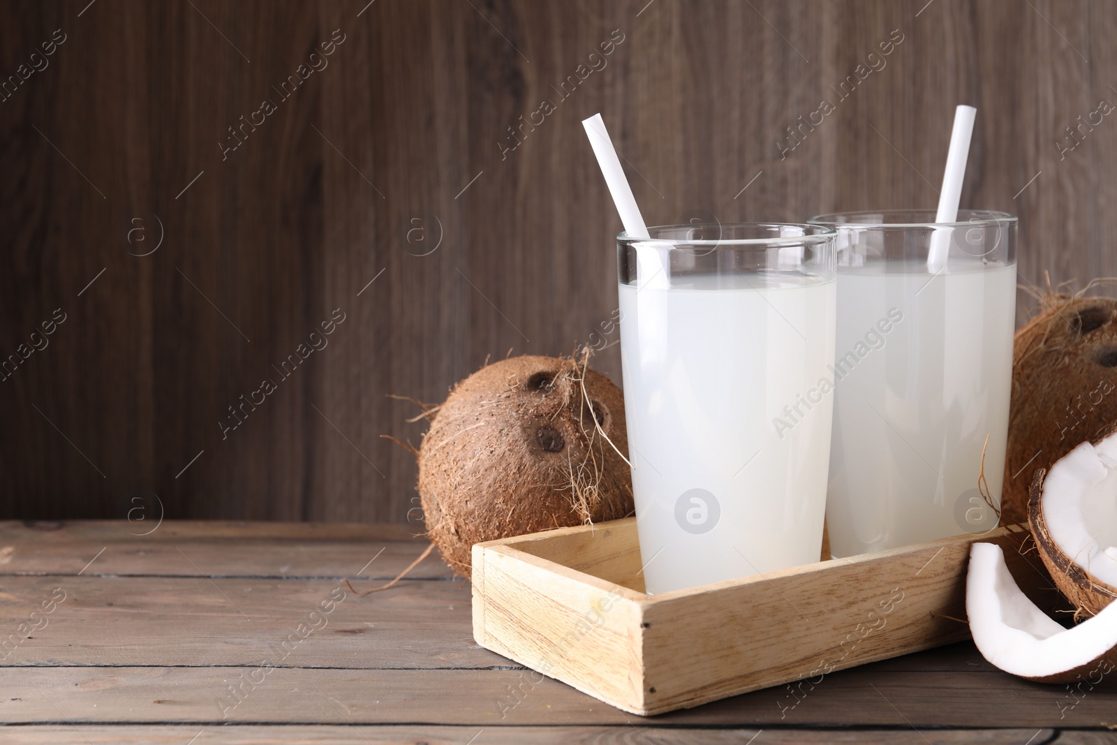 Photo of Glasses of coconut water with straws and nuts on wooden table, space for text