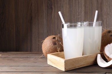 Photo of Glasses of coconut water with straws and nuts on wooden table, space for text