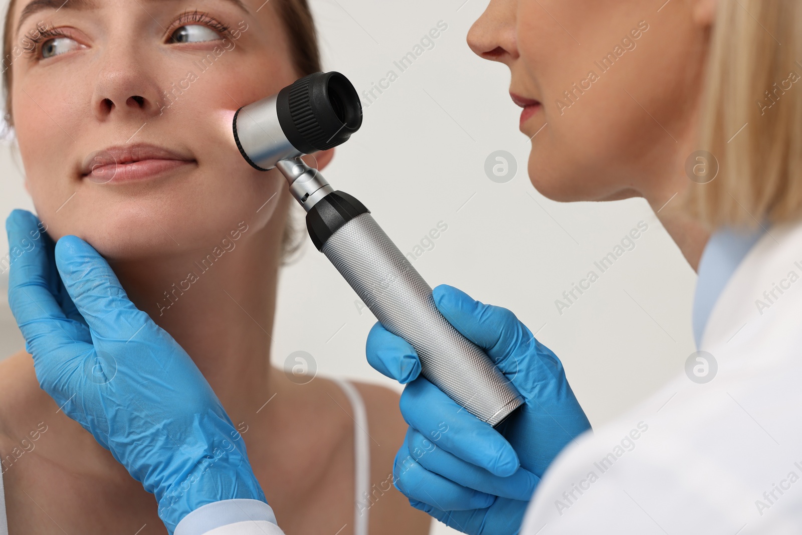 Photo of Dermatologist with dermatoscope examining patient`s face in clinic, closeup